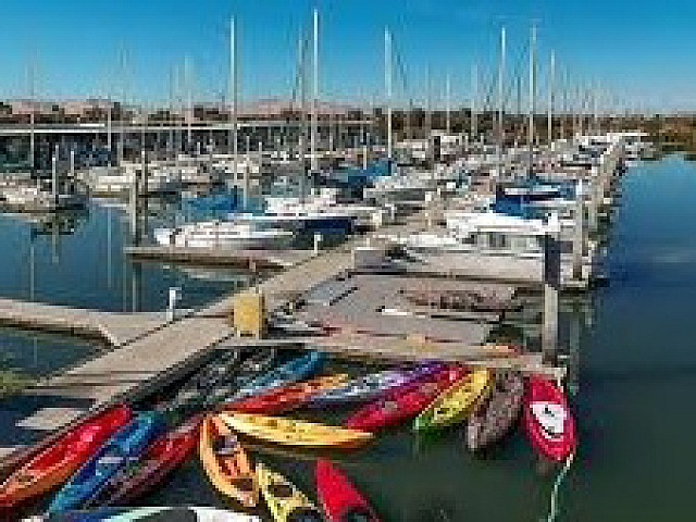 Vibrant marina scene with colorful kayaks and sailboats under a clear blue sky, offering a perfect waterfront lifestyle.