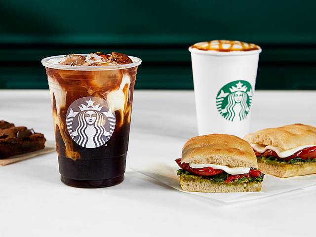 Delicious array featuring an iced coffee, cappuccino with caramel drizzle, gourmet ciabatta sandwiches, and a rich brownie on a sleek marble table.