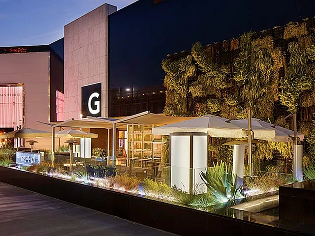 Vibrant and modern outdoor setting at a stylish shopping center, featuring lush greenery and glowing ambience under evening lights.