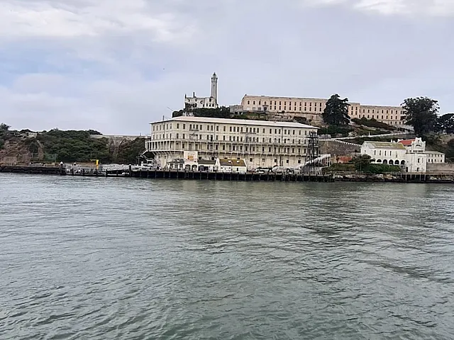Breathtaking waterfront view of historic island fortress, surrounded by lush greenery and serene waters under a cloudy sky.