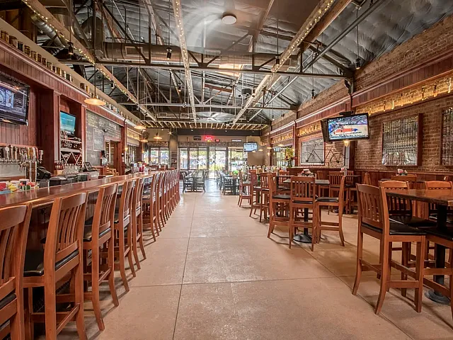 Inviting restaurant with rustic brick walls, a long wooden bar, and ample seating under an industrial-style ceiling.