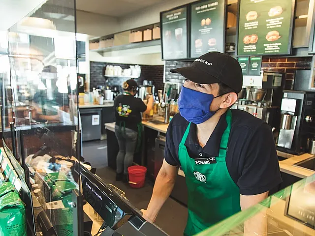 Barista in a vibrant coffee shop setting, wearing a green apron and providing friendly service.