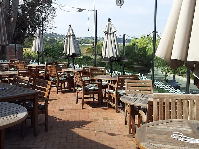 Charming outdoor patio with wooden tables and umbrellas, surrounded by lush greenery and offering scenic views.