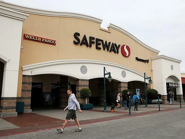 Vibrant entrance of a bustling shopping center featuring Safeway and Wells Fargo with people strolling past.