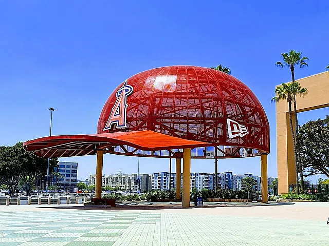 Vibrant outdoor landmark featuring a giant red baseball cap structure with a scenic backdrop of modern apartments and lush palm trees.