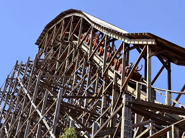 Exciting wooden roller coaster with thrilling drops and happy riders against a clear blue sky.