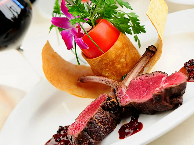 Gourmet lamb chops elegantly plated with rich sauce, complemented by a vibrant garnish and accompanied by a glass of fine red wine.