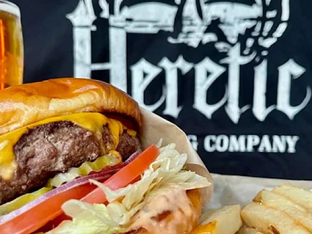 Mouthwatering cheeseburger with fresh toppings, crispy fries, and a cold beer, showcasing Heretic Brewing Company's delicious offerings.
