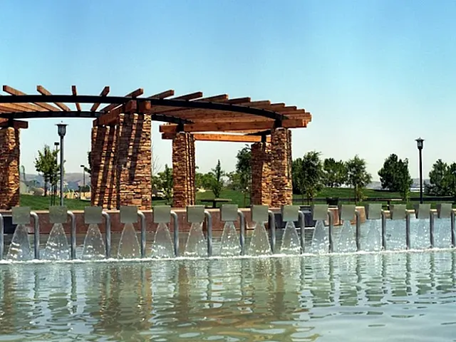 Stunning outdoor water feature with cascading fountain and elegant stone pergola, surrounded by lush greenery and clear blue skies.