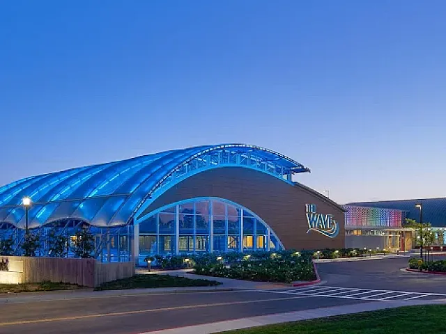 Stunning modern building with a unique wave-inspired glass facade illuminated in vibrant blue lights during twilight.