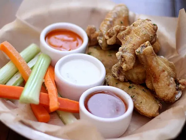 Delicious platter of crispy chicken wings served with vibrant carrots, celery sticks, and a trio of flavorful dipping sauces.