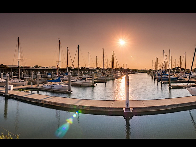 Vibrant marina scene with colorful kayaks and sailboats under a clear blue sky, offering a perfect waterfront lifestyle.