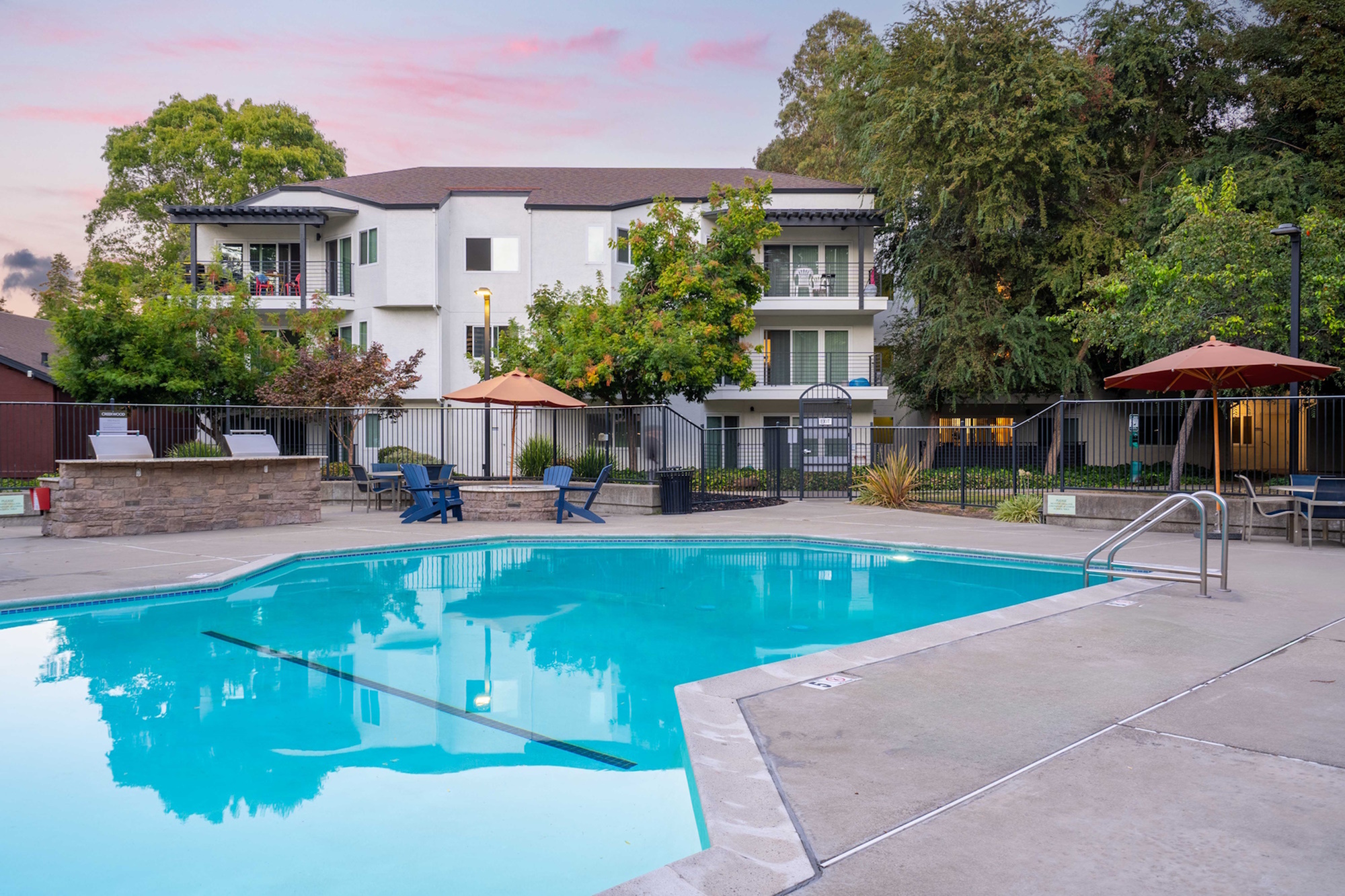 Modern apartment complex with a sparkling pool, surrounded by greenery and outdoor seating.