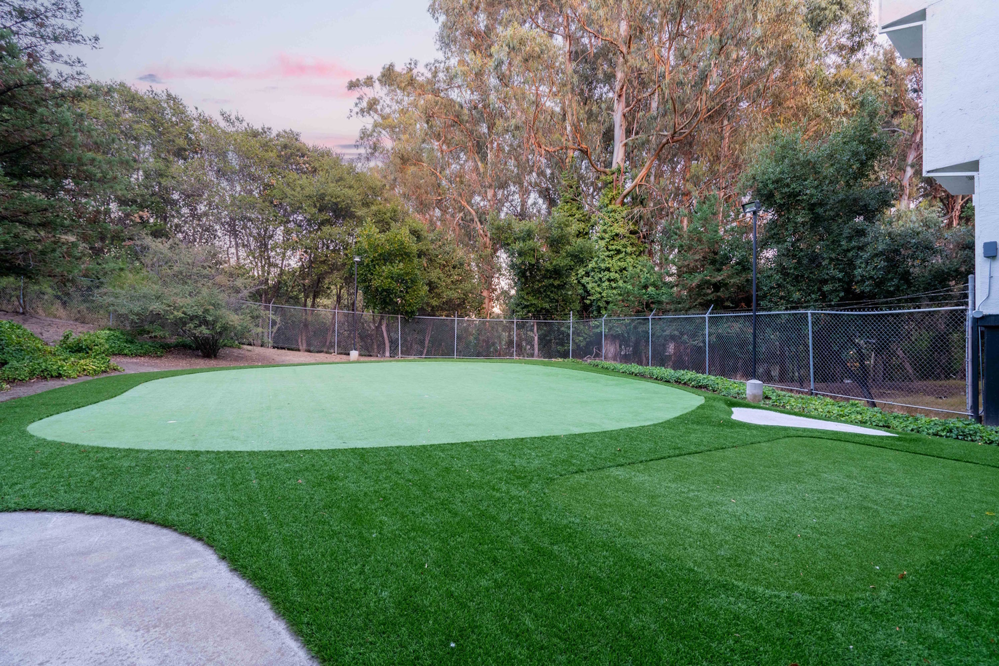 Peaceful putting green landscape with well-maintained artificial turf surrounded by lush trees and a secure fence, ideal for relaxation and leisure.