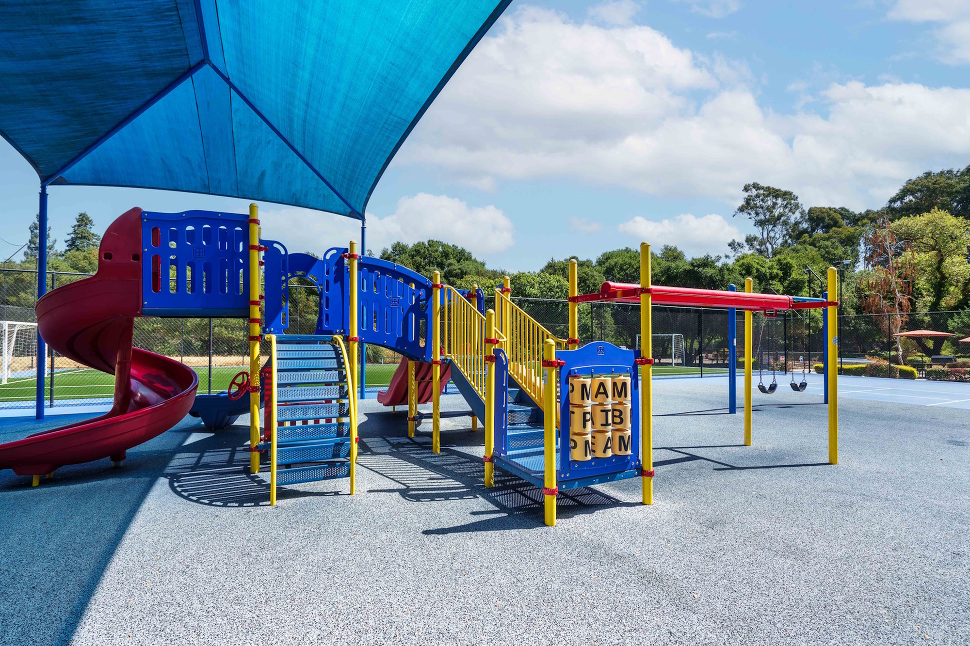 Colorful playground under a shade structure with slides and swings.