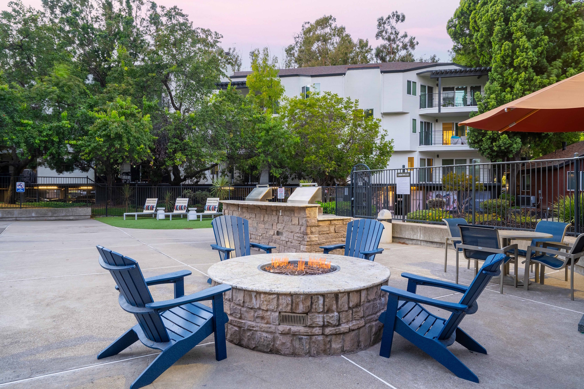 Modern apartment community with inviting outdoor fire pit and seating area, surrounded by lush greenery.