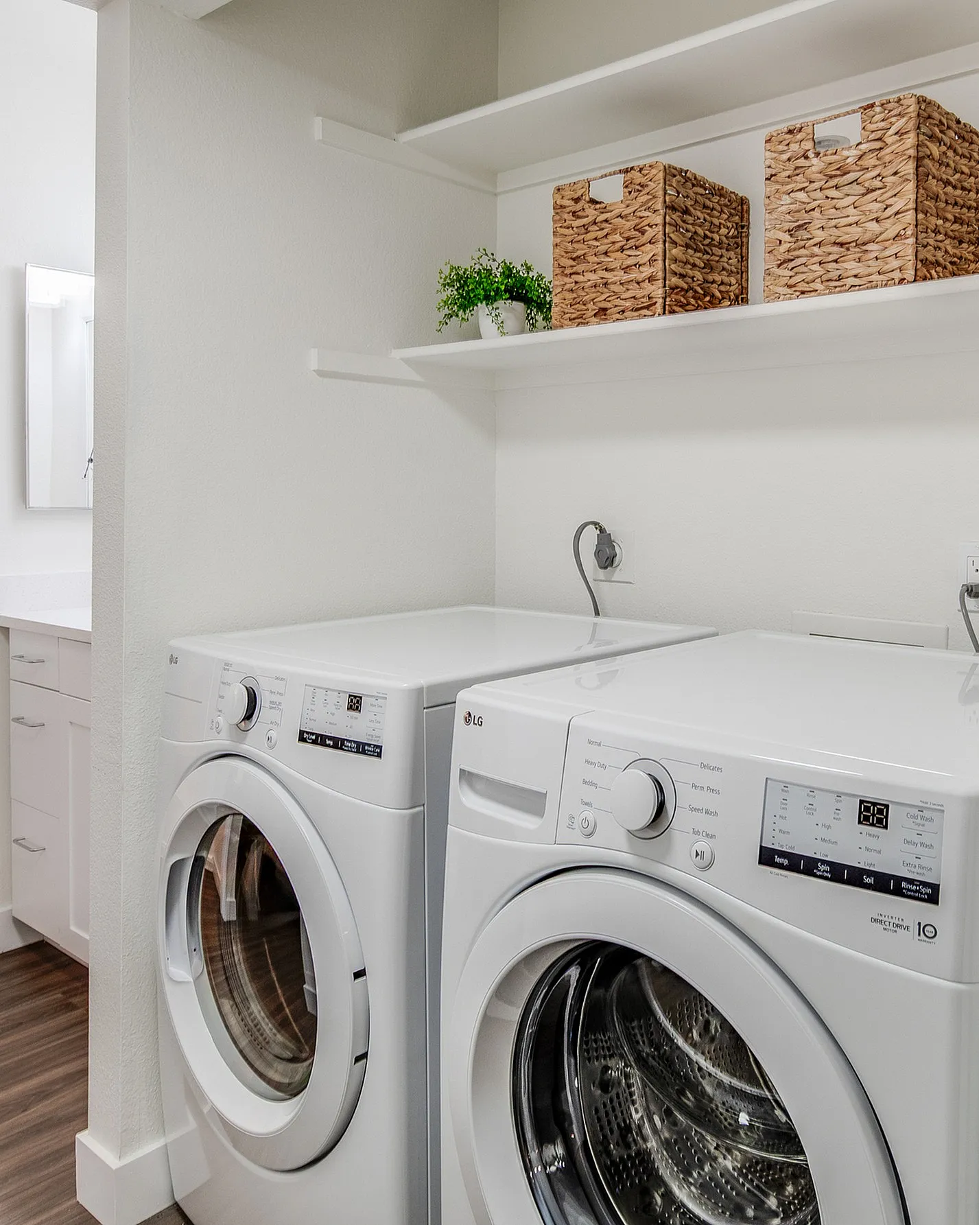 Modern laundry room featuring sleek white washer and dryer, stylish wicker storage baskets, and a touch of greenery on open shelves.