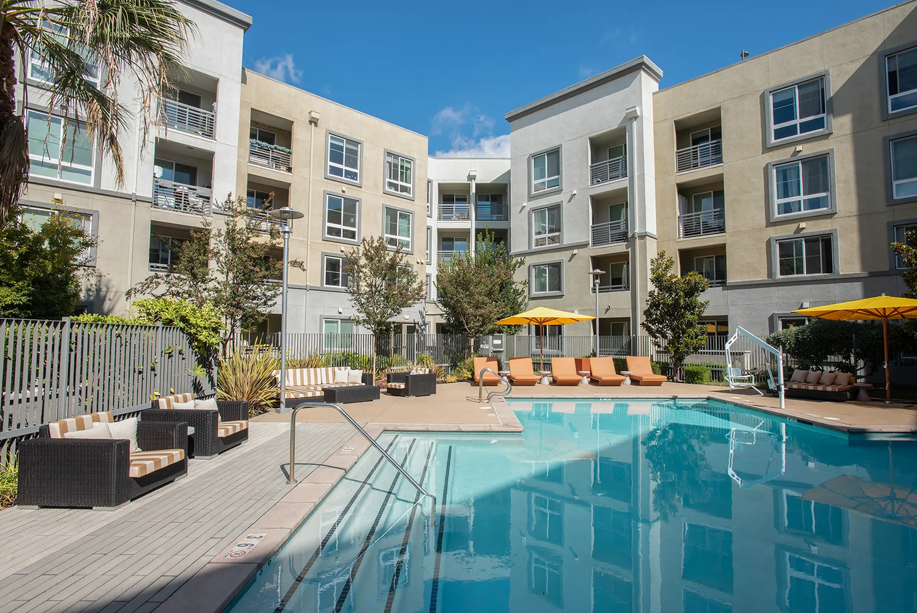 Chic apartment complex showcasing a pristine outdoor pool surrounded by modern lounge chairs and sun umbrellas.