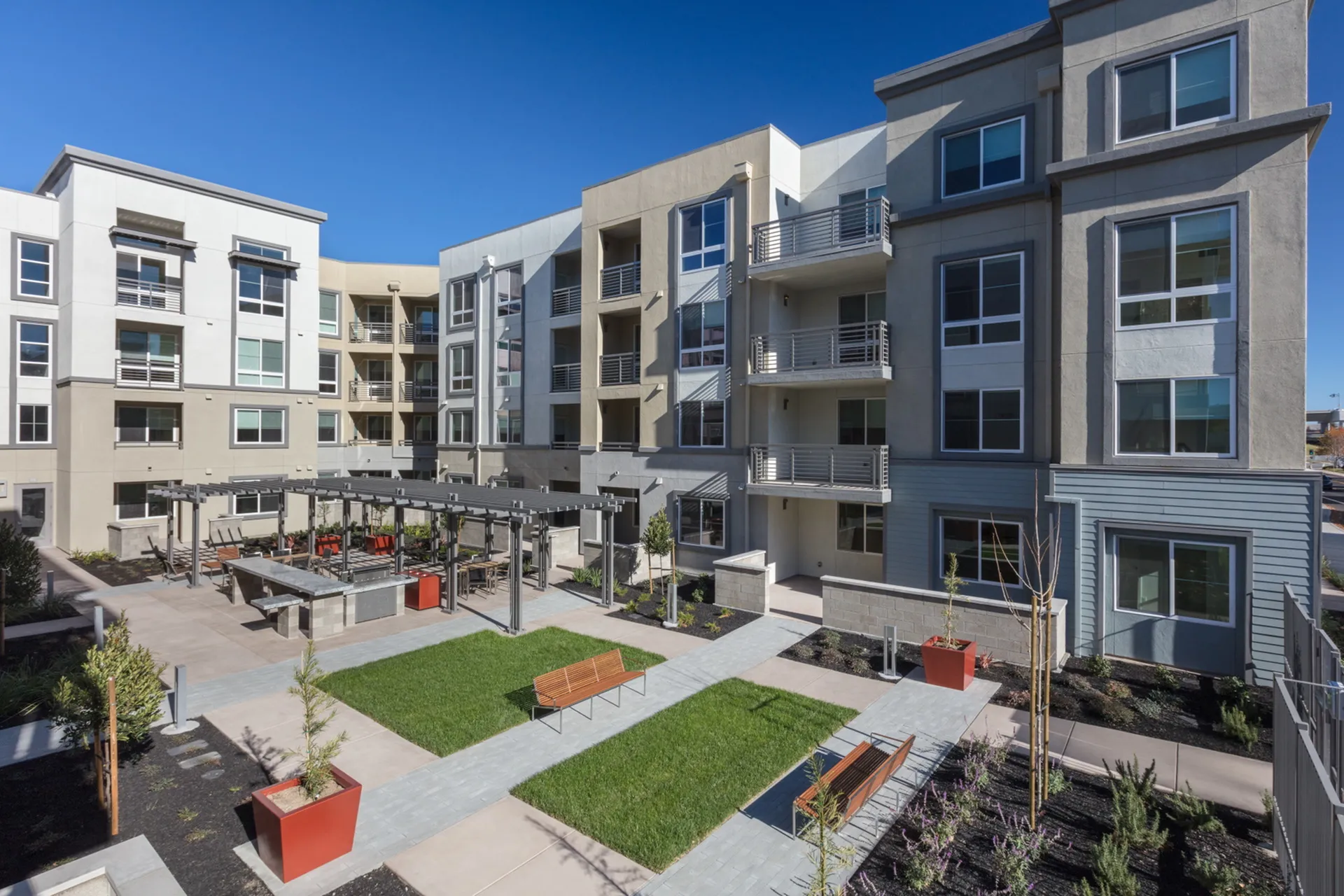 Modern apartment complex with spacious balconies, landscaped courtyard, and stylish outdoor seating in a sunny setting.