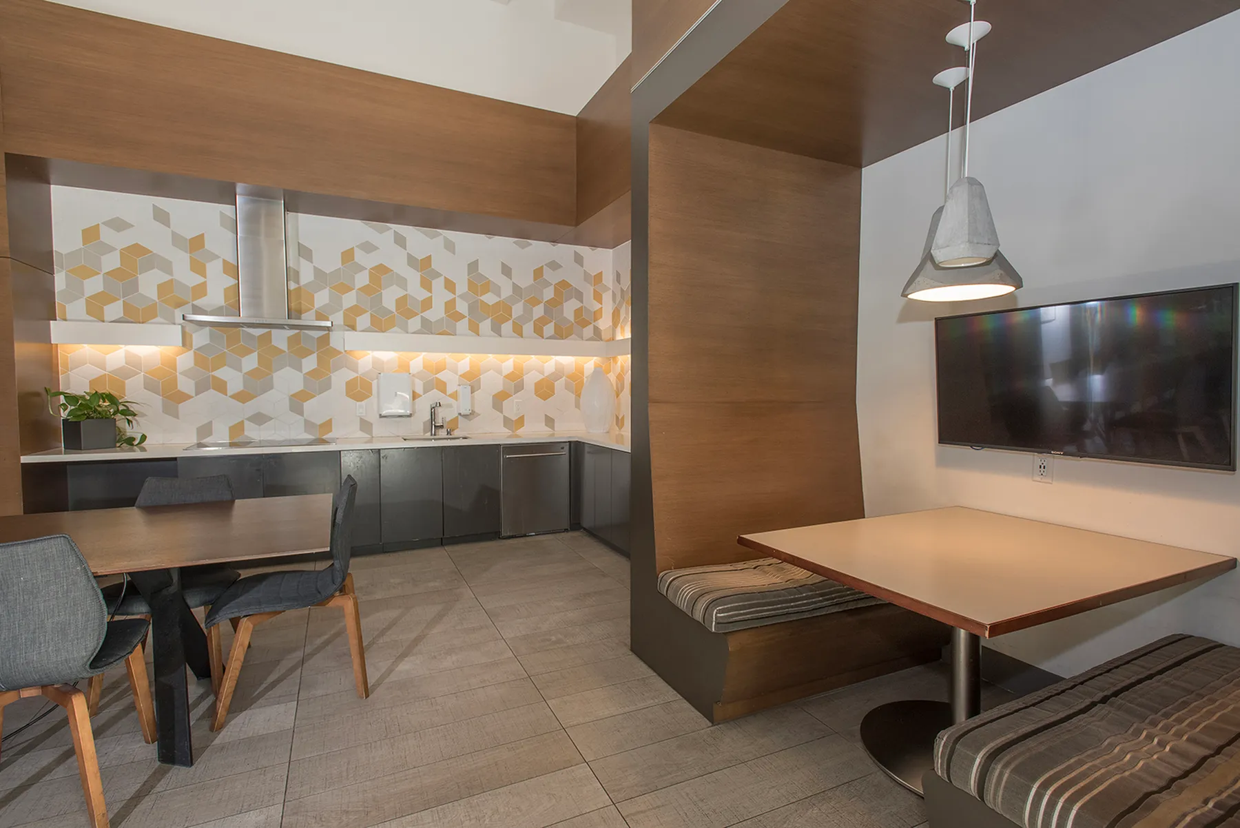 Modern kitchen and dining area featuring geometric tile backsplash, sleek cabinetry, and cozy breakfast nook with wall-mounted TV.