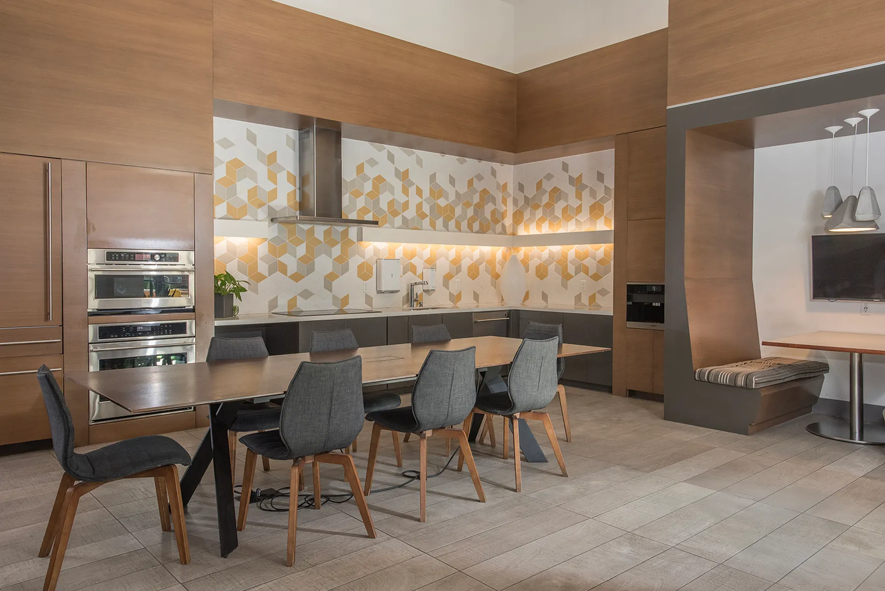 Elegant modern kitchen and dining area with wood cabinetry, geometric tile backsplash, and a large dining table with chic chairs.