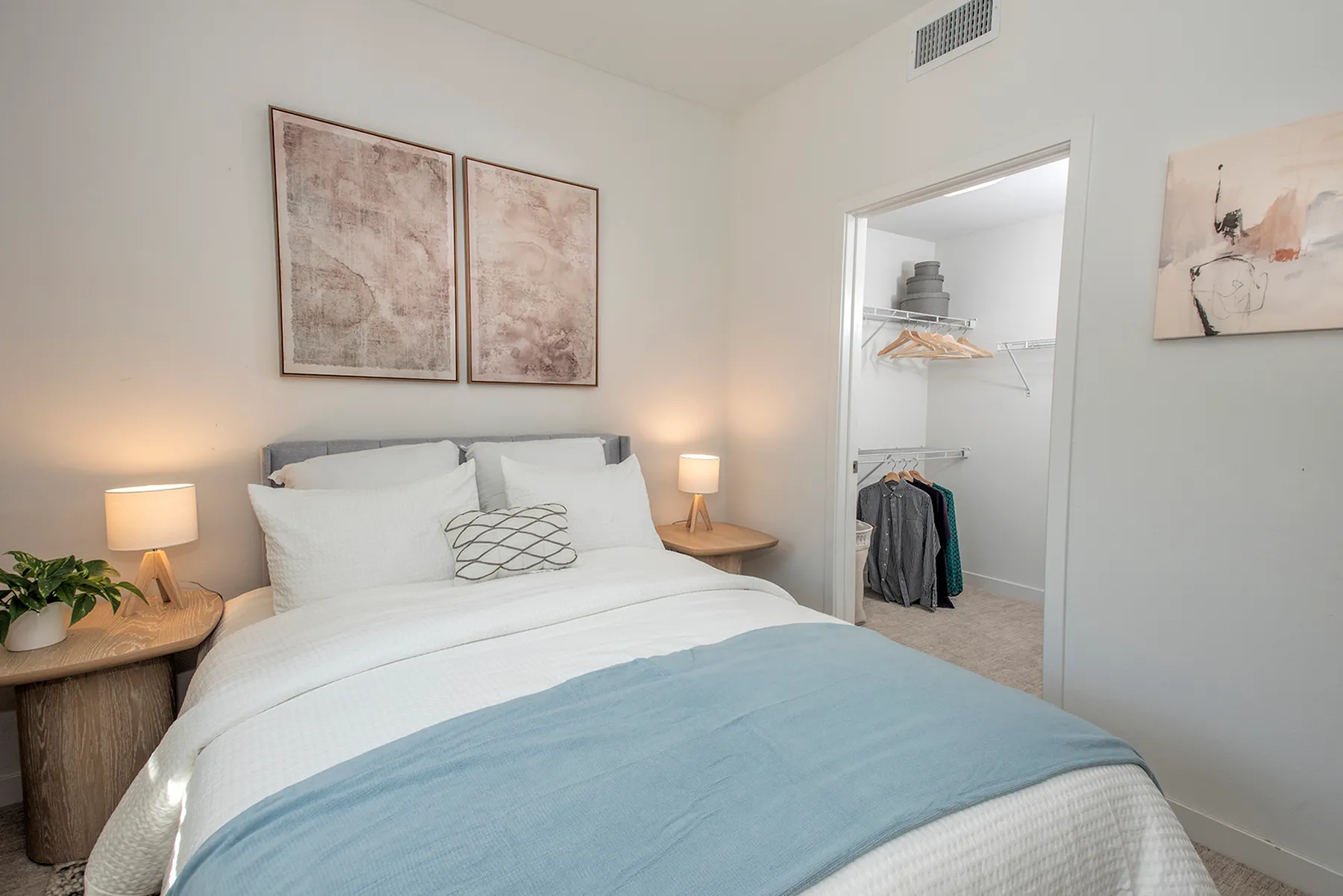 Cozy bedroom featuring elegant decor, plush bedding, modern artwork, and a spacious walk-in closet with ample storage.