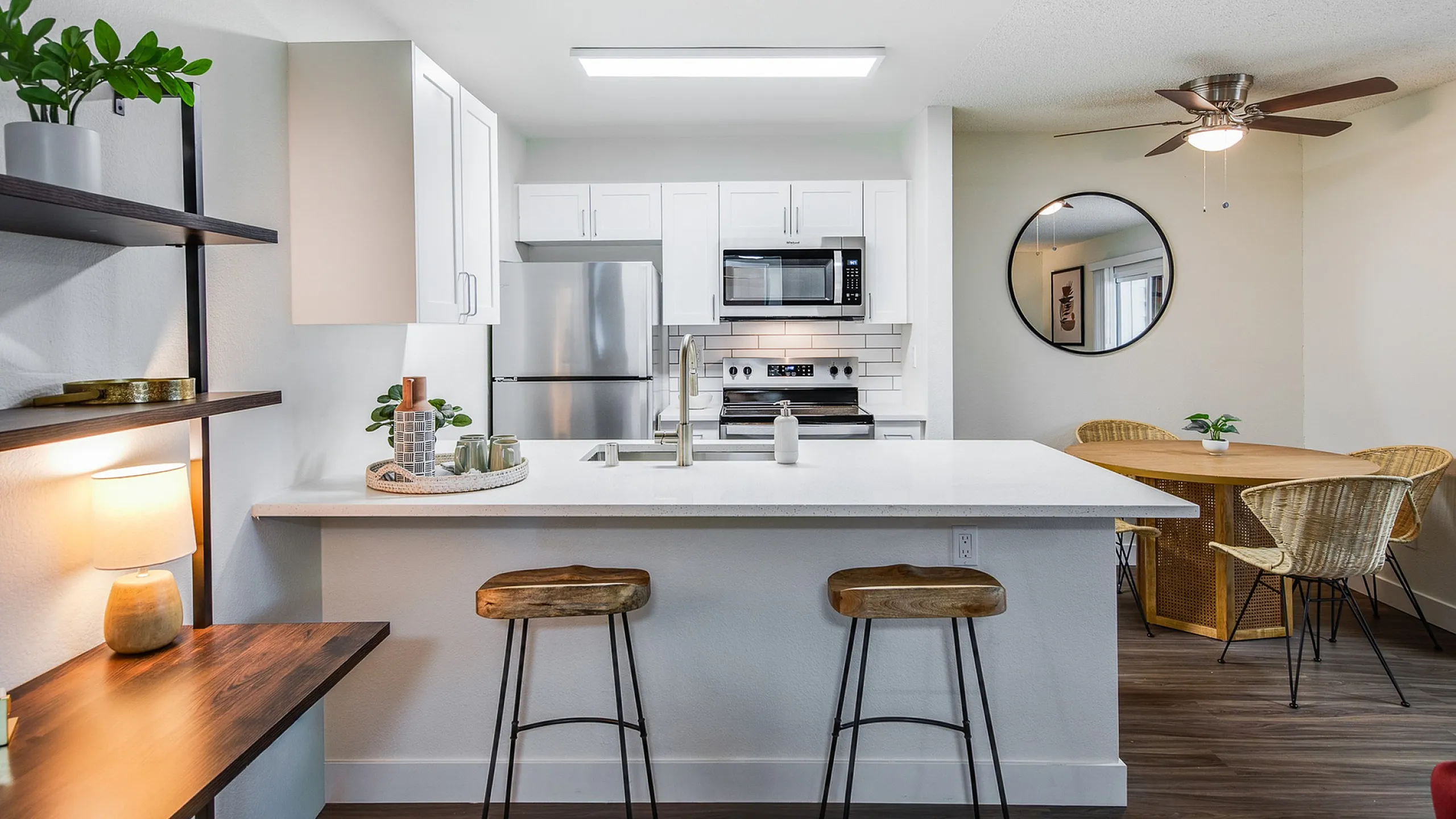 Modern kitchen with sleek white cabinets, stainless steel appliances, and a cozy breakfast bar with wooden stools, adjacent to a chic dining area with rattan chairs.