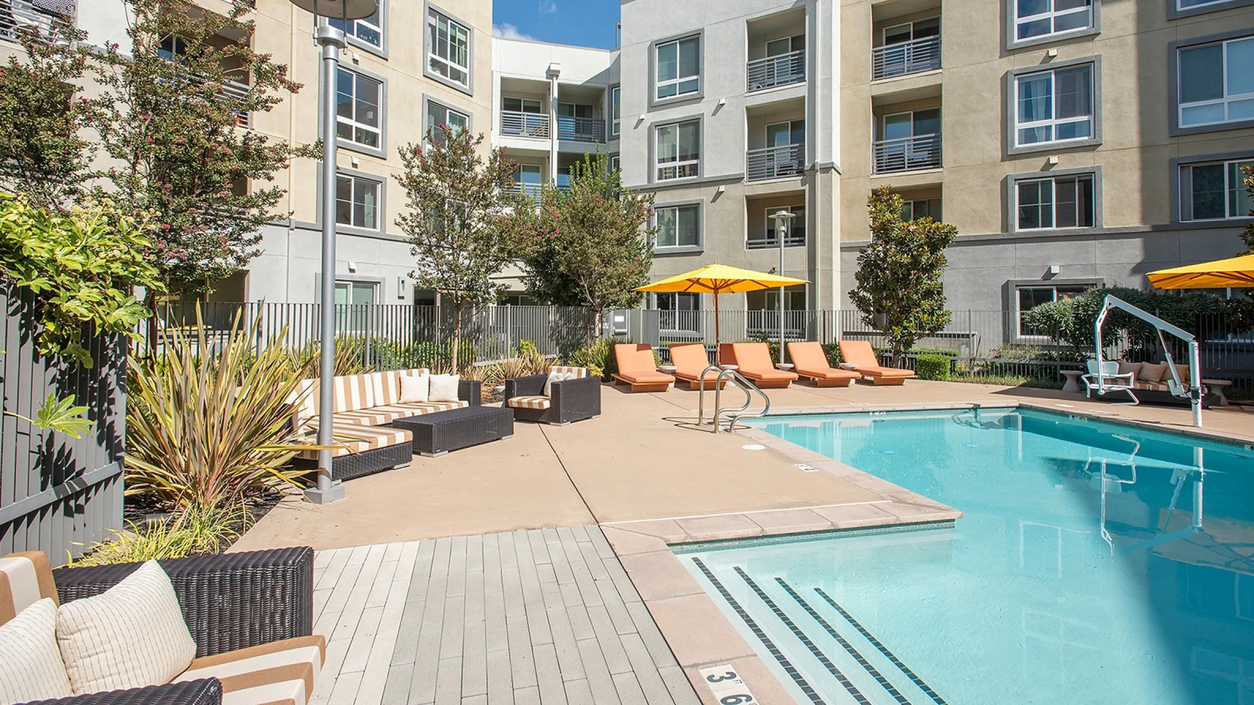 Inviting apartment complex with a sparkling pool, stylish lounge chairs, and modern architecture surrounded by lush greenery.