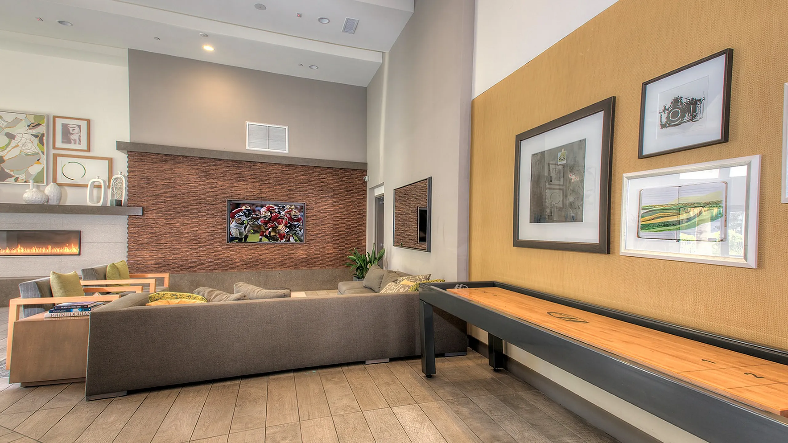 Inviting modern living room boasting a sleek fireplace, cozy sofas, and dynamic sports decor, complemented by elegant wall art and a stylish shuffleboard table.
