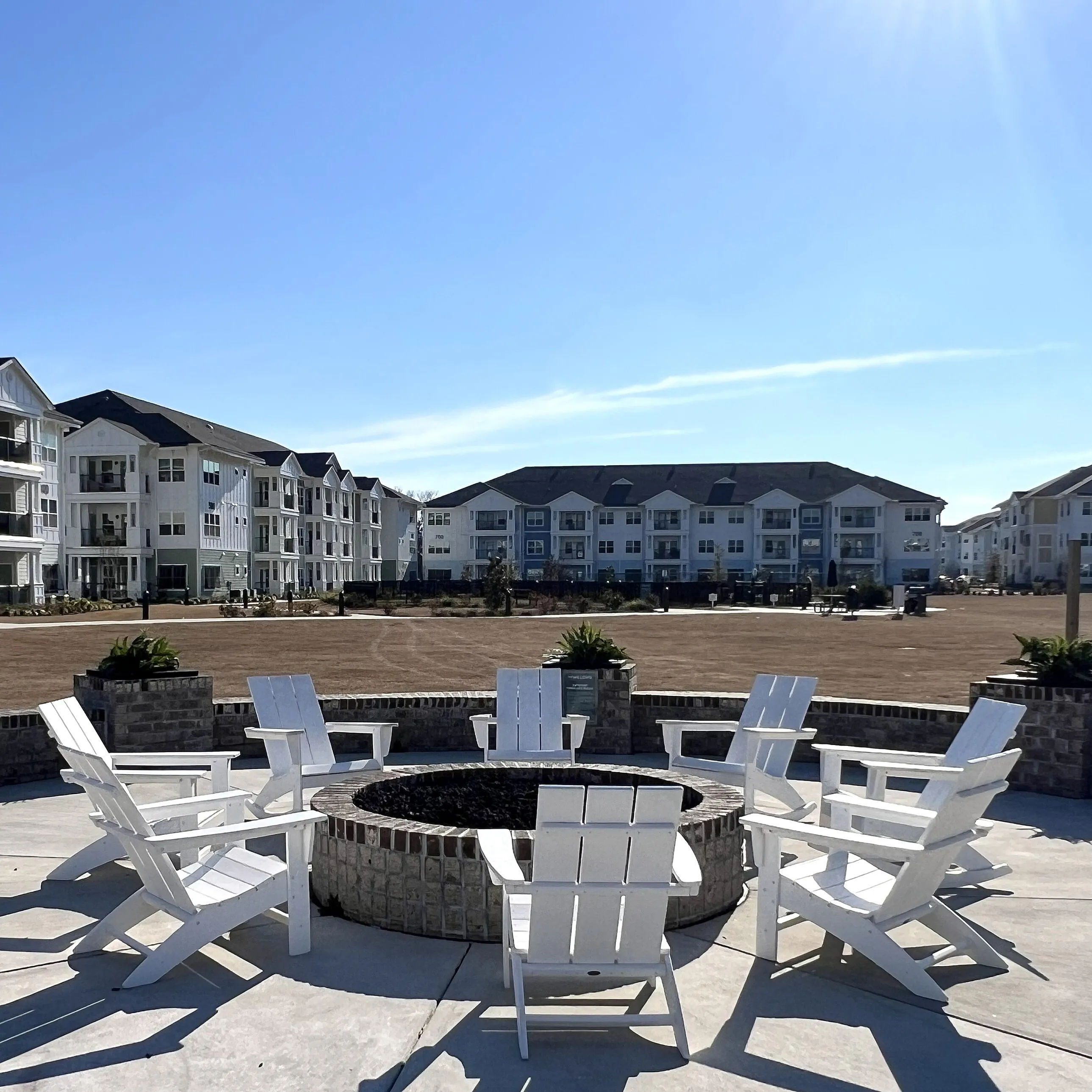 Modern apartment complex with cozy firepit seating, surrounded by spacious green areas and outdoor recreation facilities.