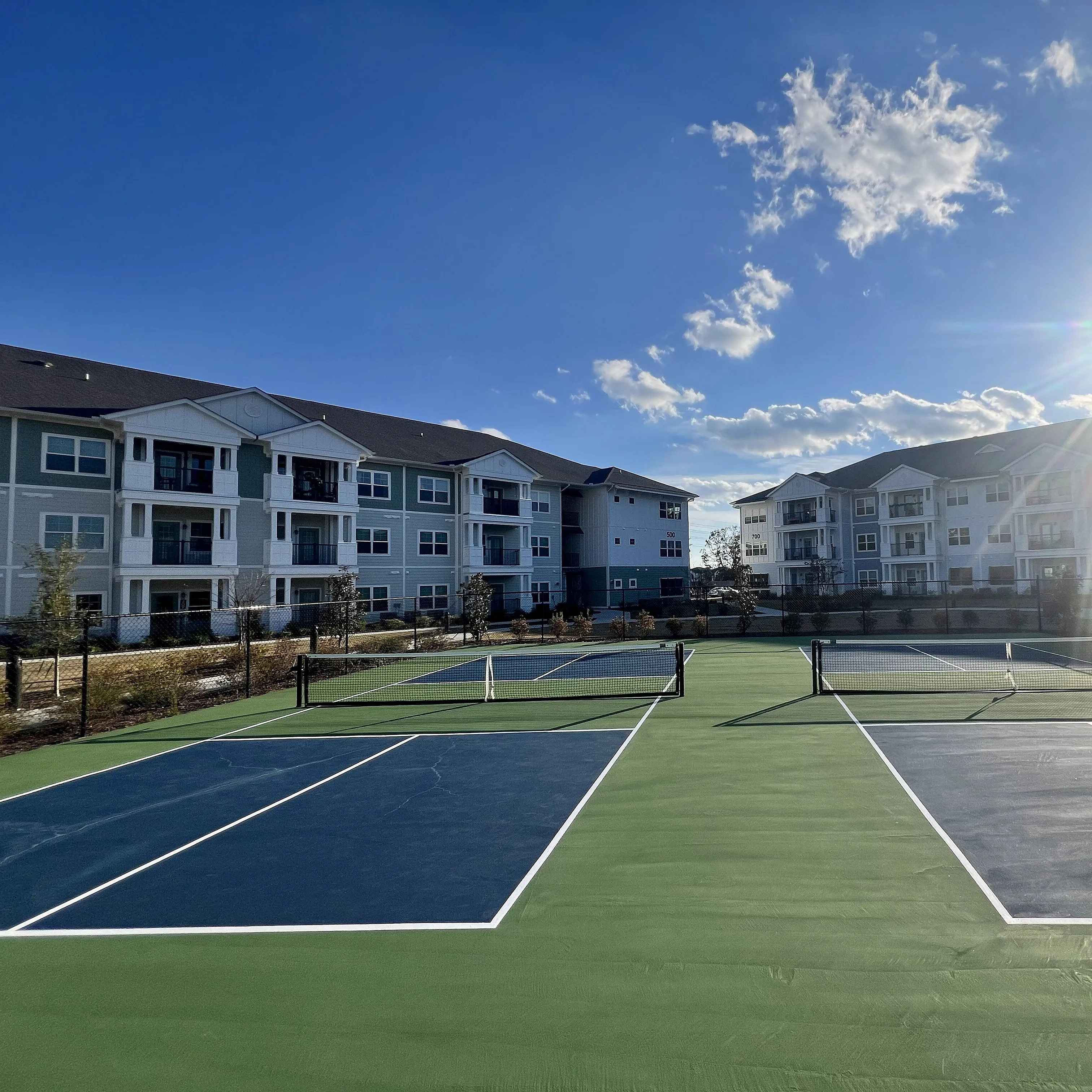 Modern apartment complex with spacious balconies, nestled alongside inviting tennis courts under a bright, sunny sky.