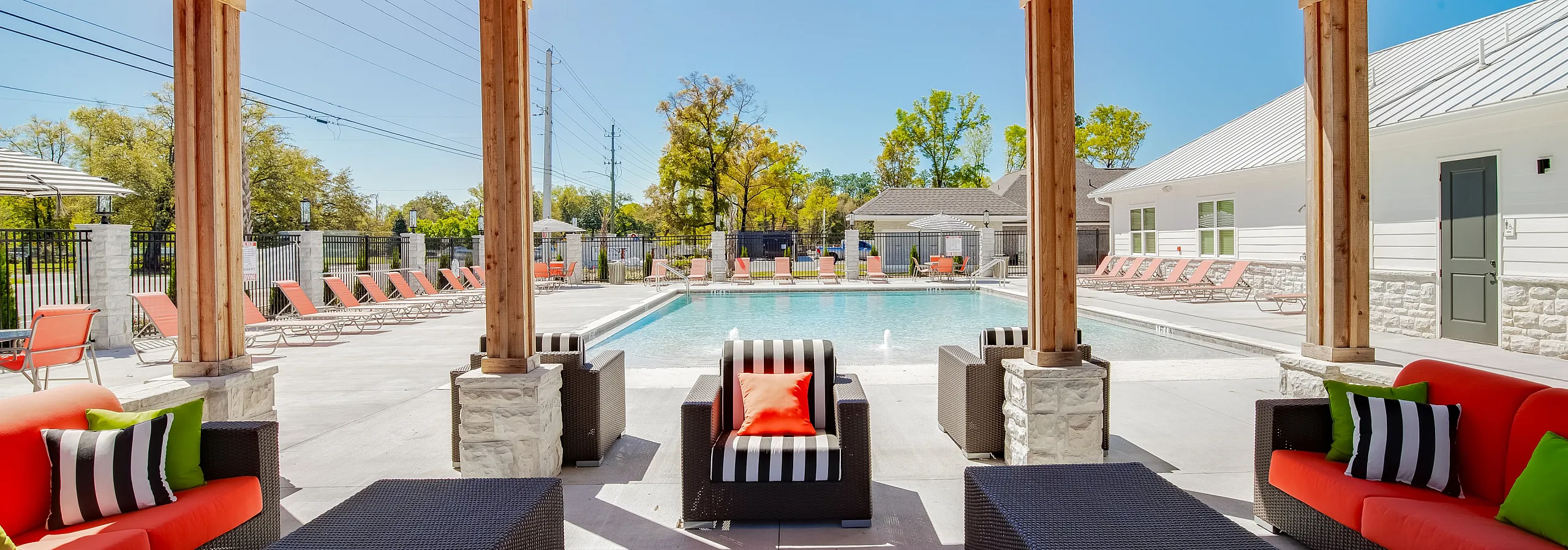 Luxurious outdoor lounge area with modern seating under a wooden pergola, overlooking a sparkling pool lined with chic orange loungers.