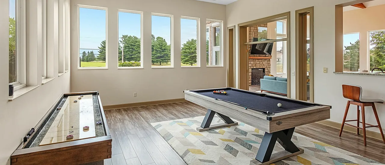 Bright and airy game room with floor-to-ceiling windows, featuring a modern pool table and sleek shuffleboard, perfect for entertaining.