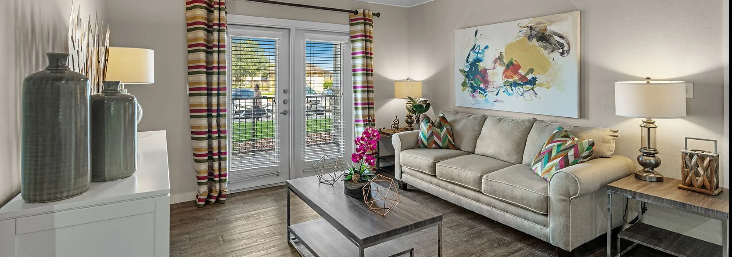 Chic living room with modern decor, featuring a stylish sofa, elegant artwork, and a cozy coffee table, illuminated by natural light from glass doors.