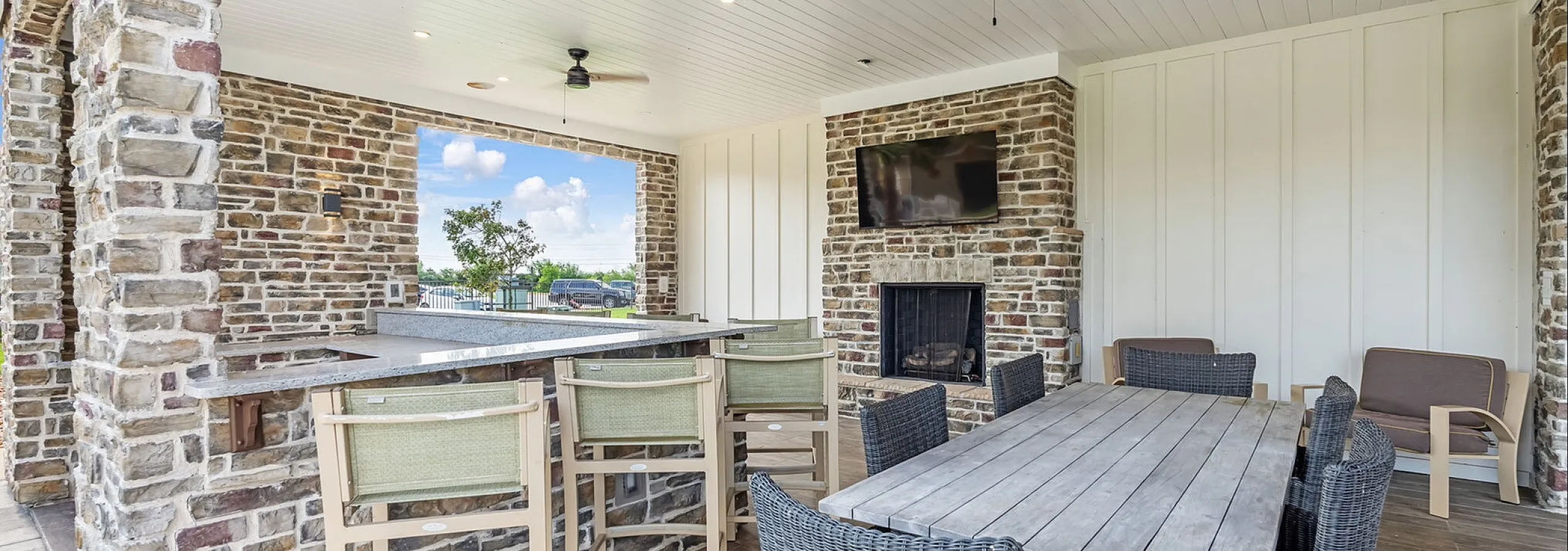 Charming outdoor patio features elegant stone walls, a cozy fireplace, spacious seating with wicker chairs, and a sleek bar area under a bright white ceiling, ideal for entertaining.