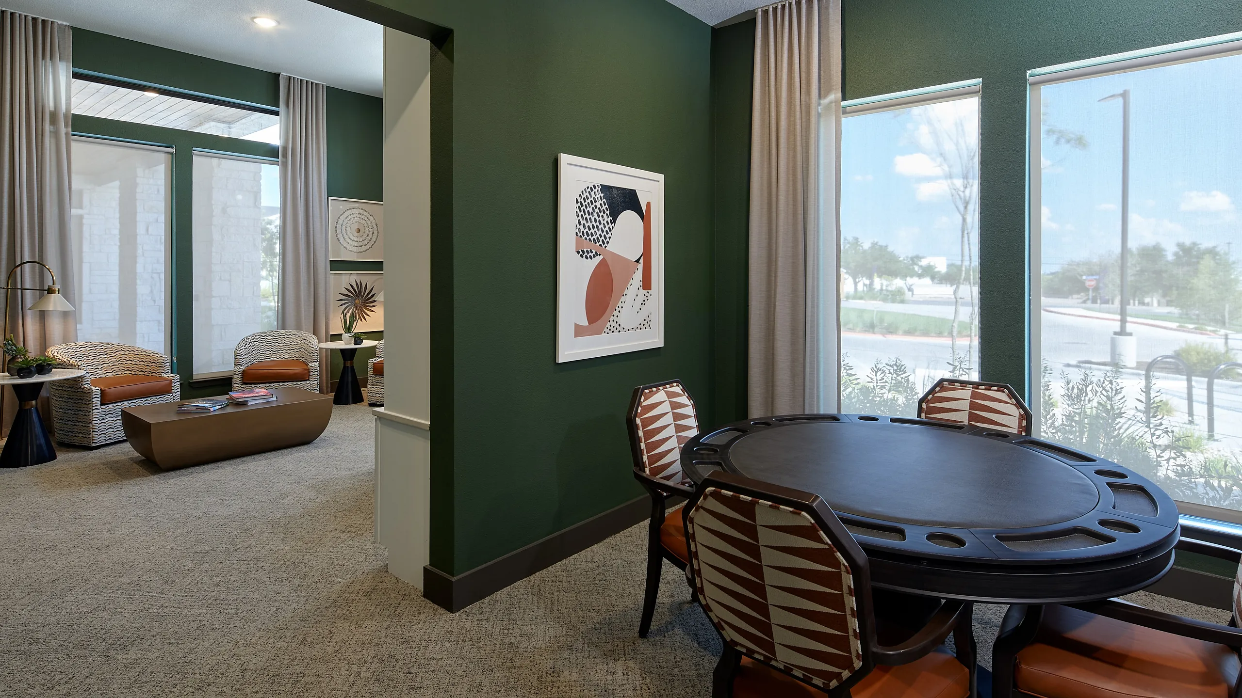 Chic interior showcasing a cozy seating area with modern wicker chairs and a stylish, green accent wall, complemented by large windows offering plenty of natural light.