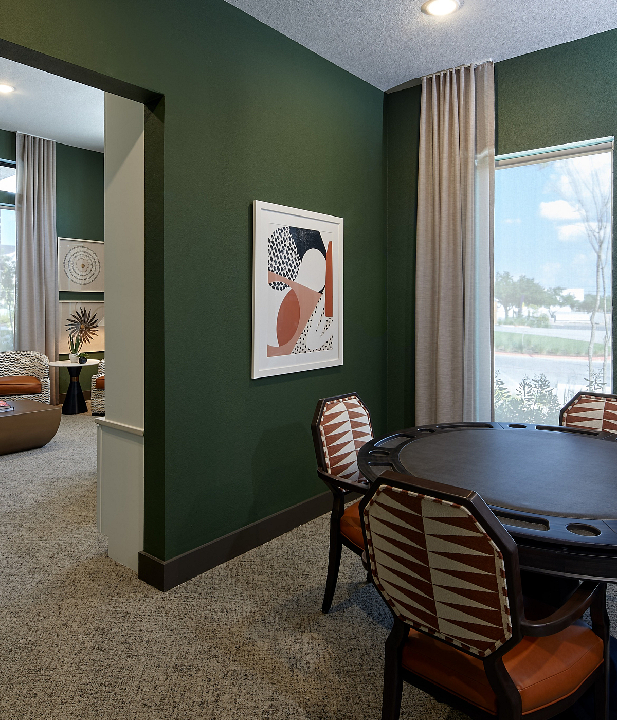 Chic seating area with stylish decor and a round table, bathed in natural light from large windows with a serene view.