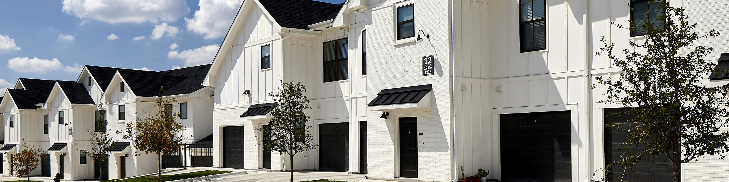 Charming row of modern townhouses with pristine white facades, black accents, and serene neighborhood setting under a bright blue sky.