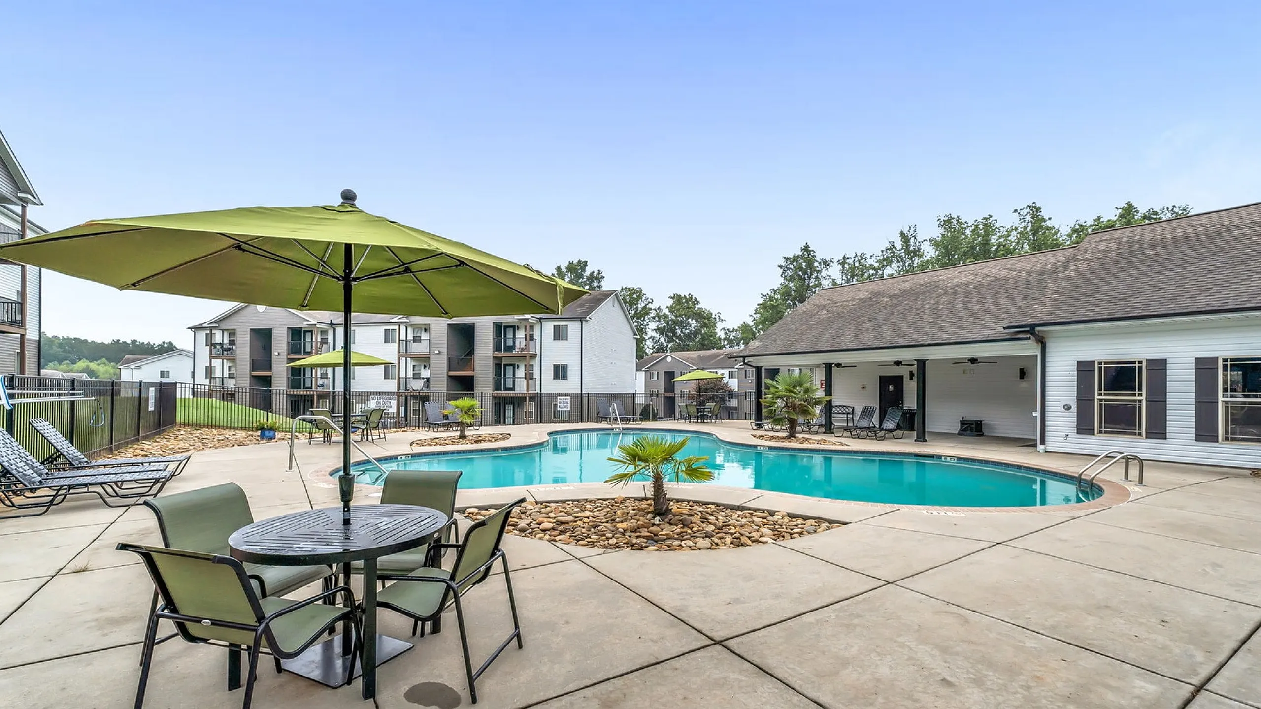 Inviting outdoor pool area with lush landscaping, modern lounge chairs, and stylish green umbrellas, perfect for relaxation and social gatherings in a vibrant apartment community.