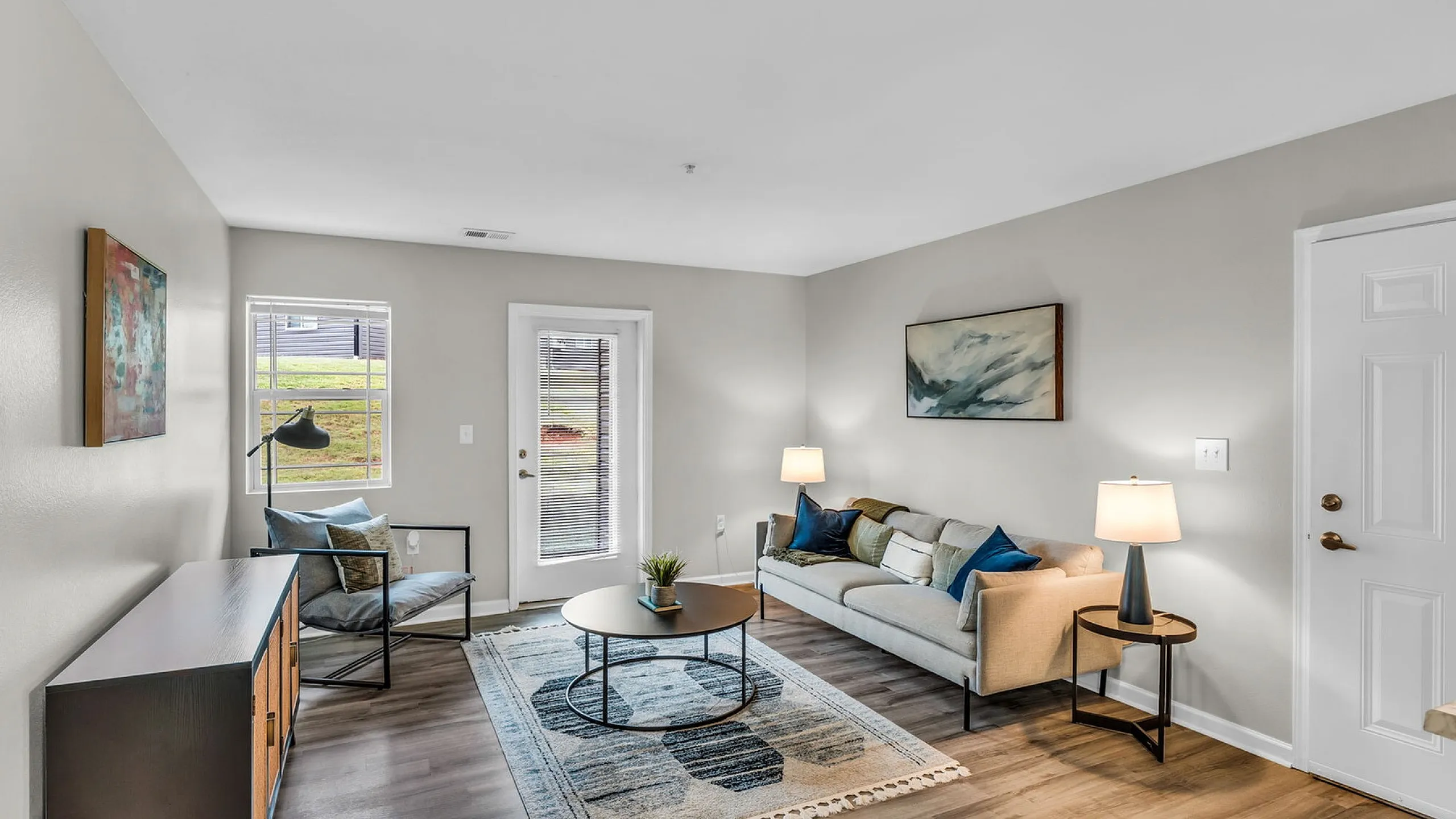 Bright and modern living room with stylish decor, cozy seating, and natural light pouring through large windows, creating an inviting space for relaxation.