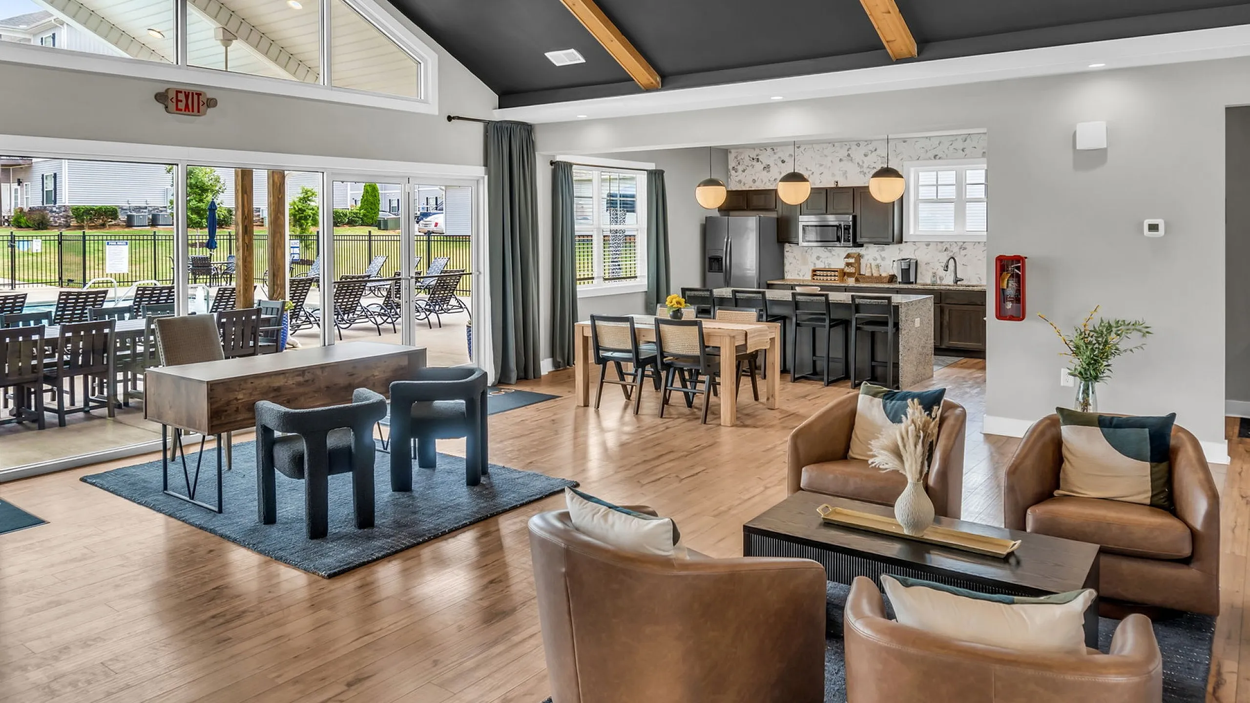 Elegant open-concept living space with modern kitchen, stylish dining area, and cozy seating, featuring large windows overlooking a poolside view.