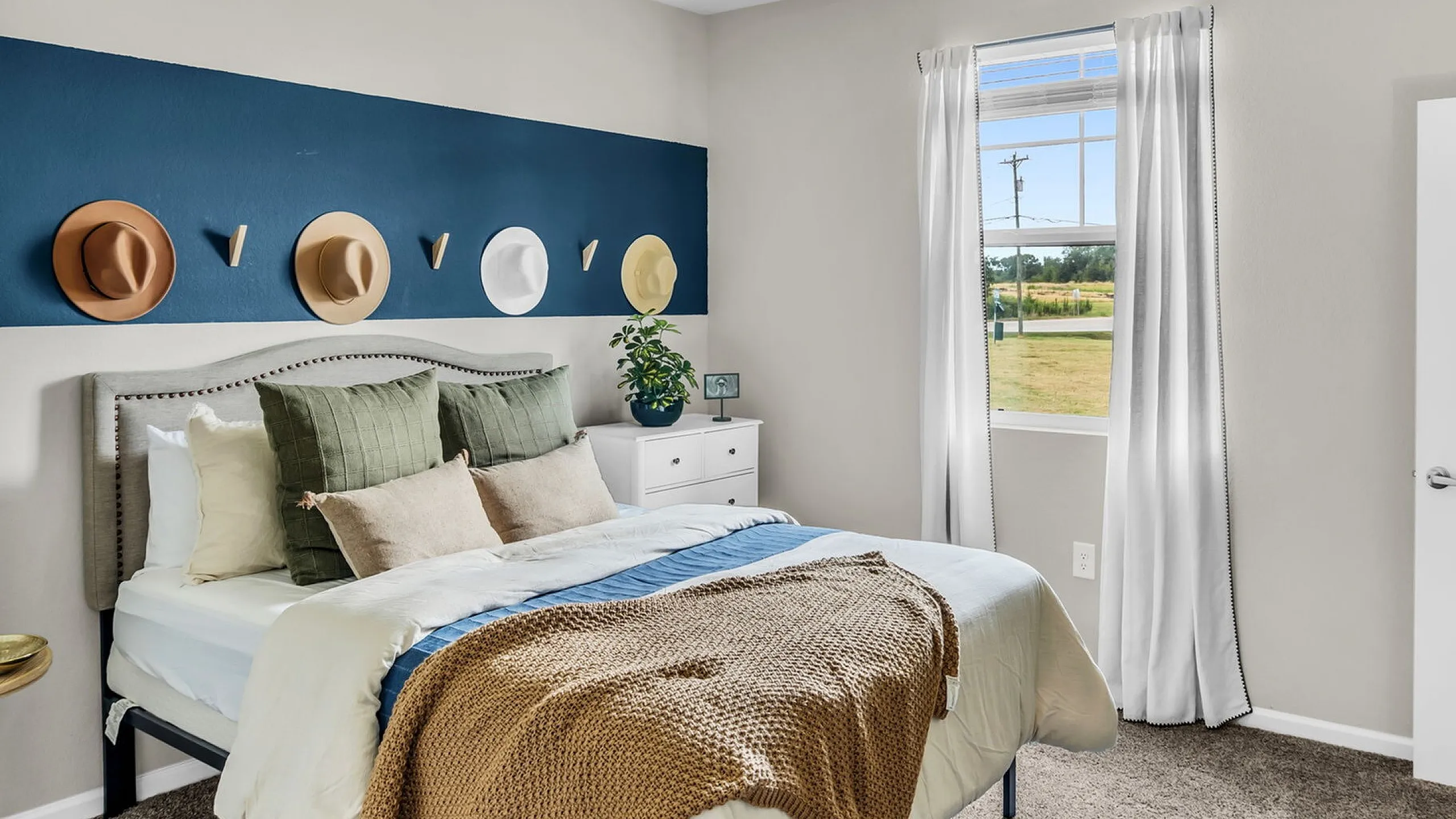 Charming bedroom with stylish hat decor, cozy bedding, and a bright window view.