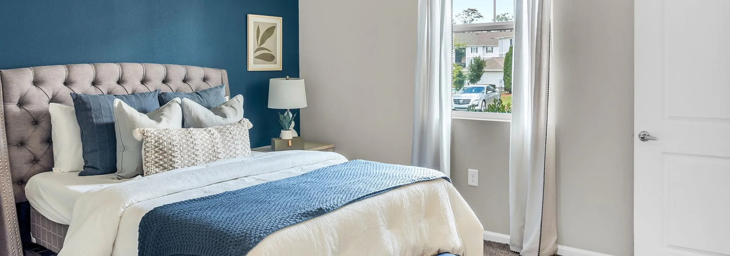 Cozy bedroom with a plush bed, navy accent wall, and bright natural lighting, perfect for relaxation.