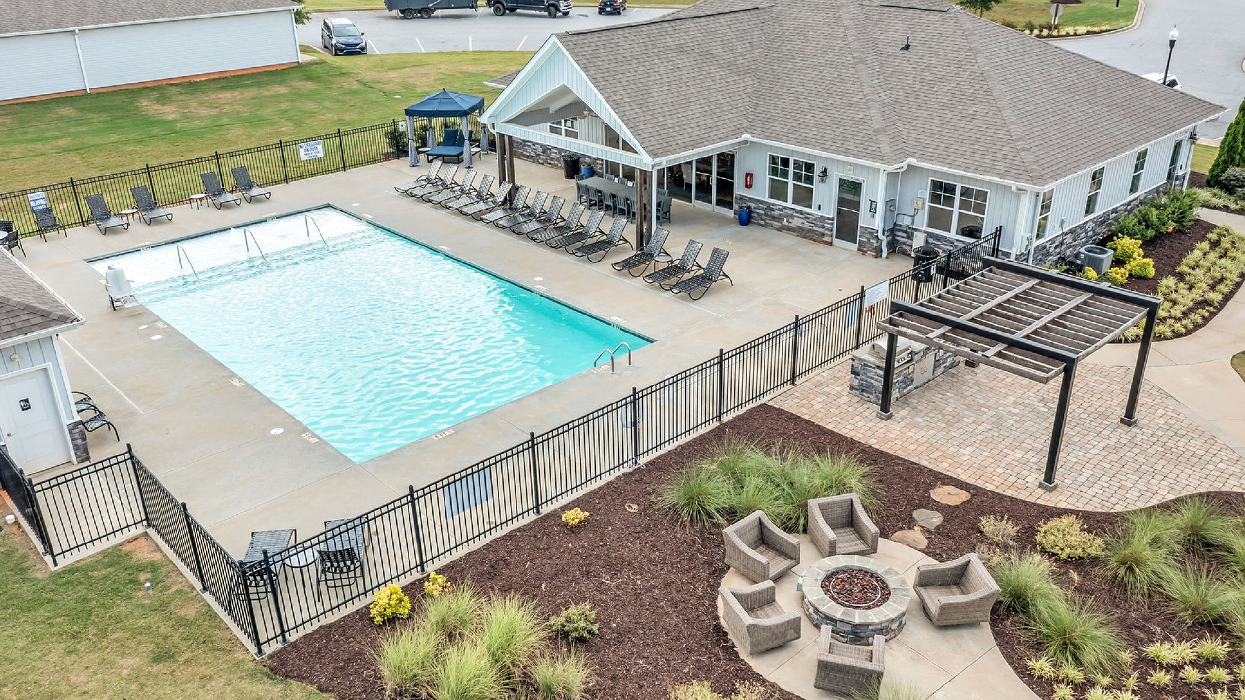 Luxurious apartment complex with a sparkling outdoor pool, ample sun loungers, and a charming fire pit area surrounded by lush landscaping.