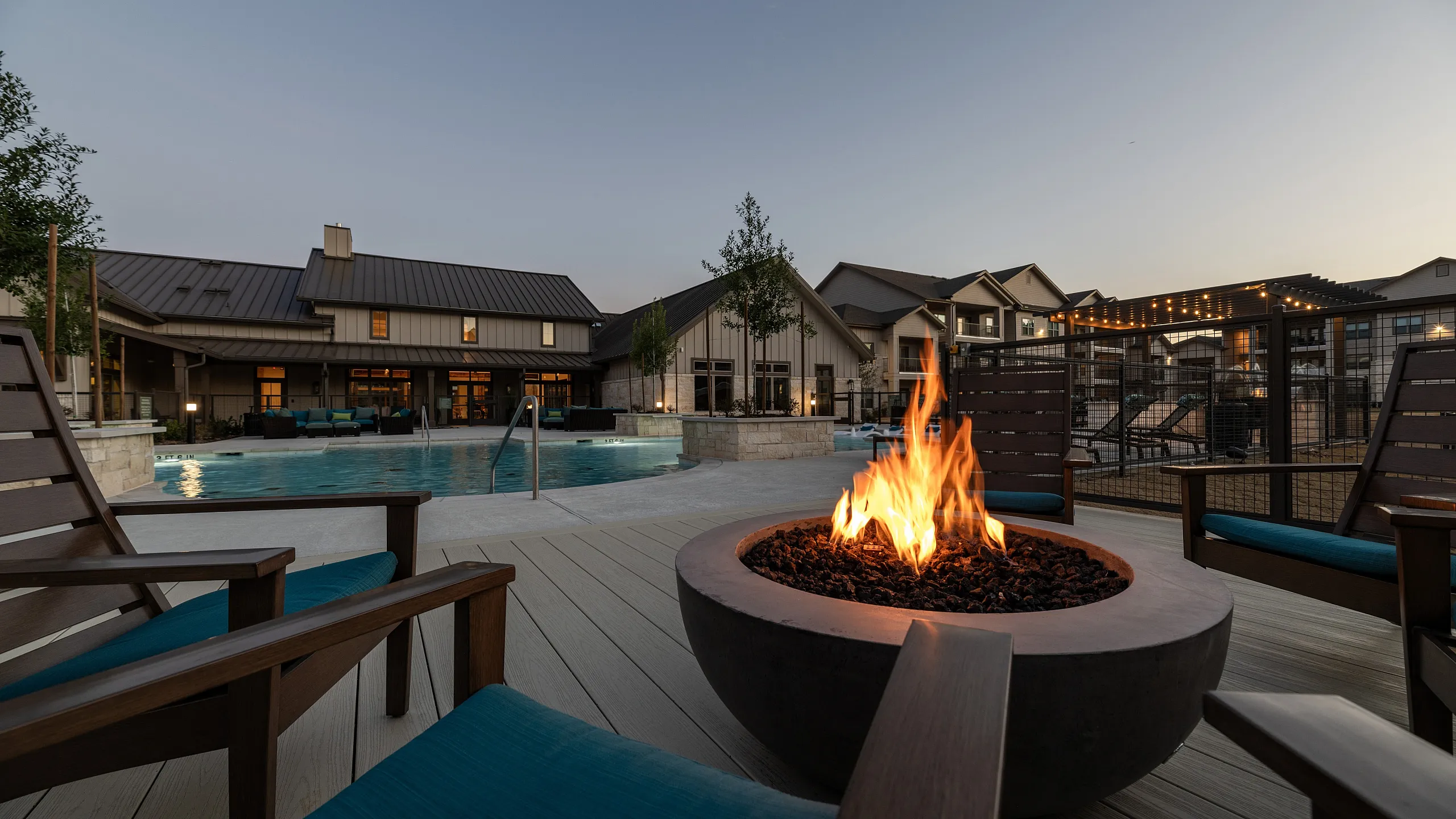 Luxurious outdoor lounge featuring a cozy fire pit, stylish seating, and a serene pool view at dusk.