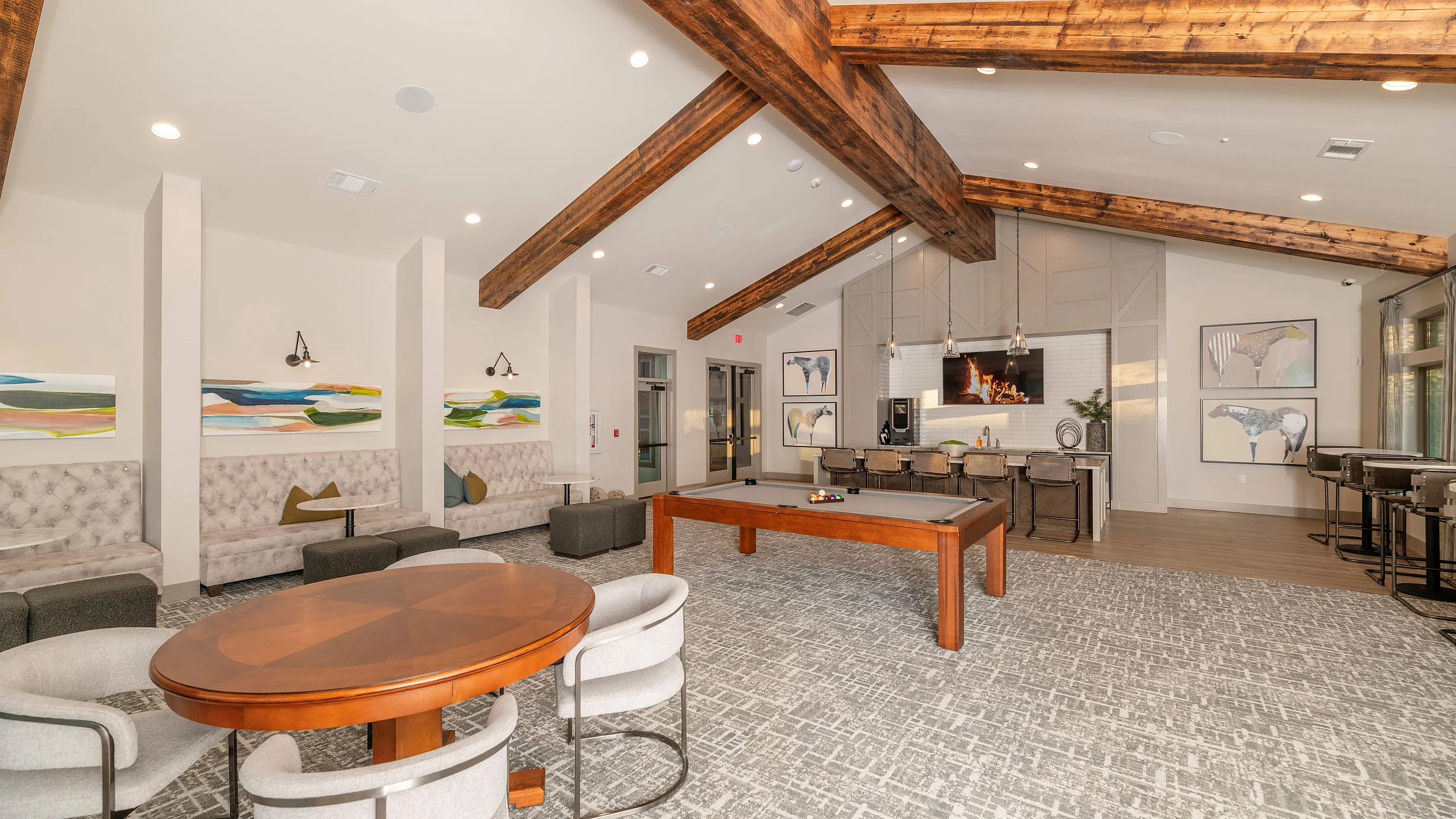 Elegant communal area featuring high wooden beam ceilings, cozy booth seating, modern art, and a pool table with inviting natural light.