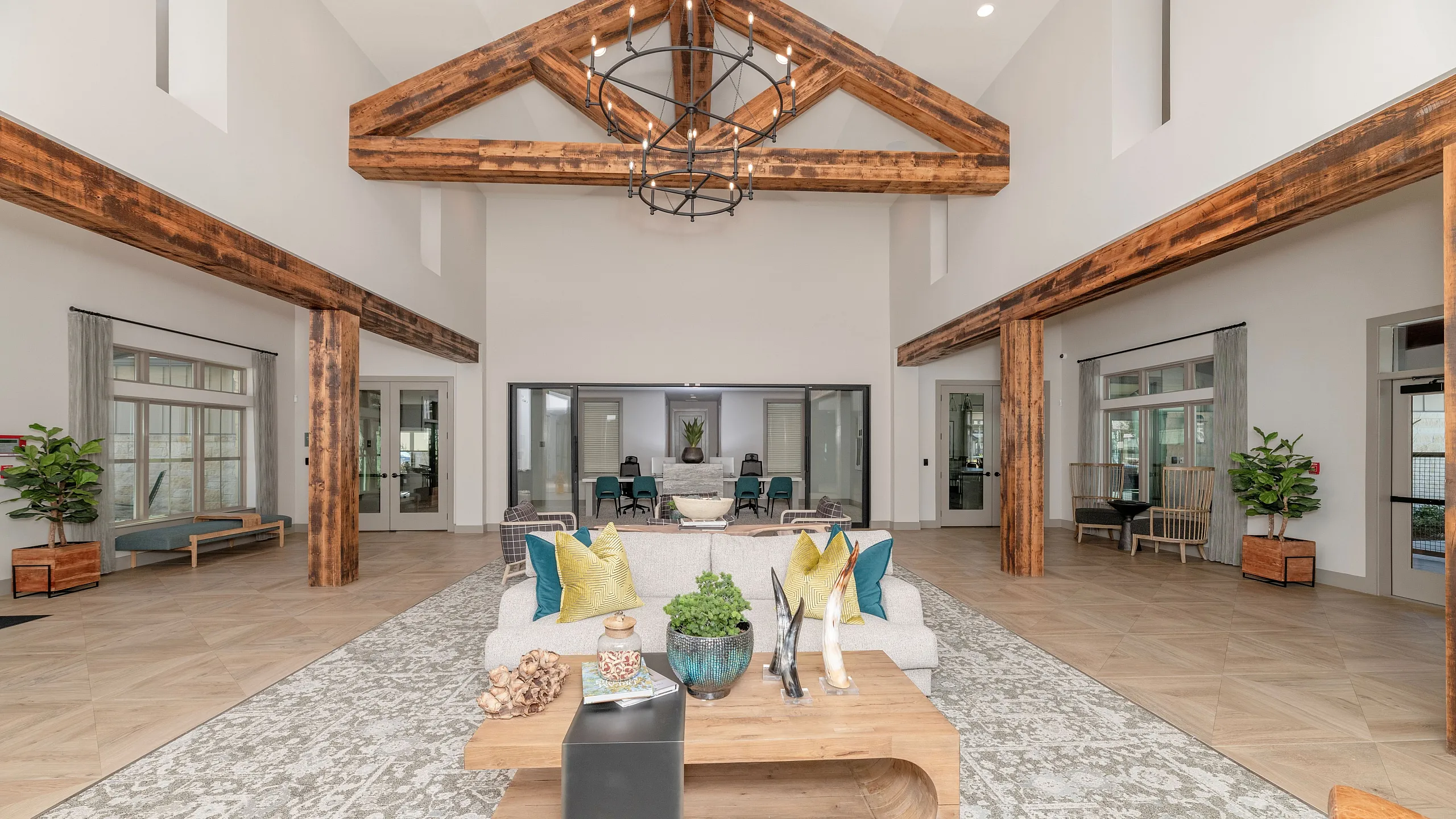 Elegant and spacious apartment lounge with rustic wood beams, stylish chandelier, and plush seating, creating a welcoming ambiance.