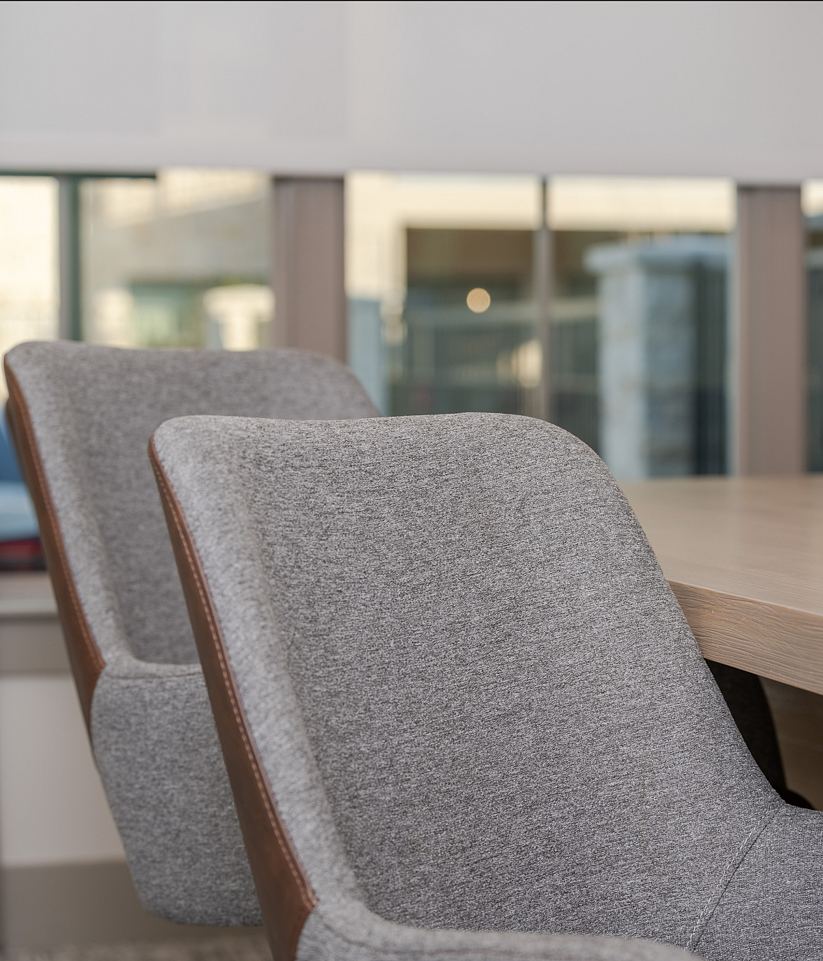 Modern conference room with elegant gray chairs and a sleek wooden table, illuminated by natural light through large windows.