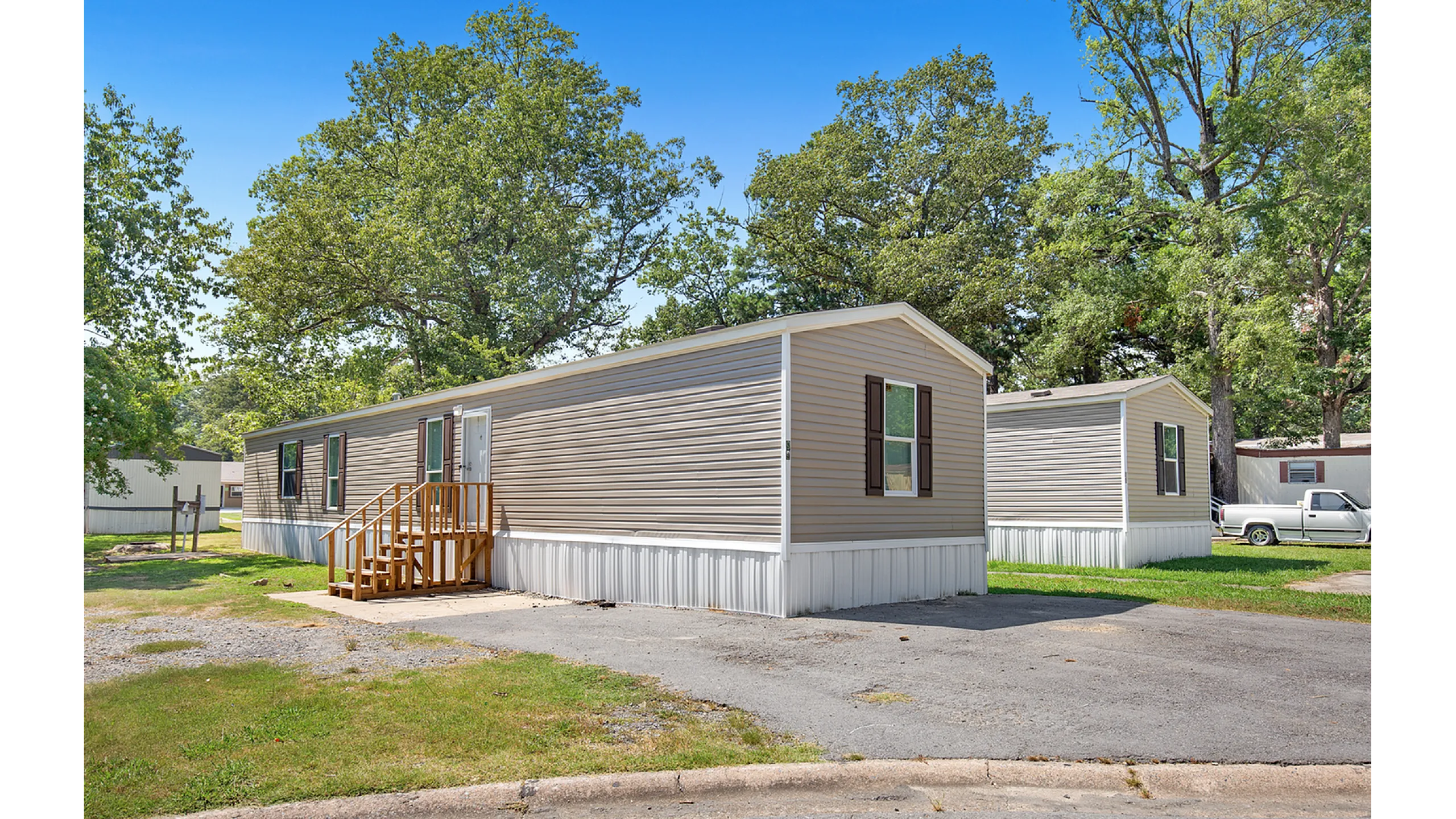 Charming mobile home nestled in a peaceful community setting, surrounded by lush greenery and a spacious driveway.