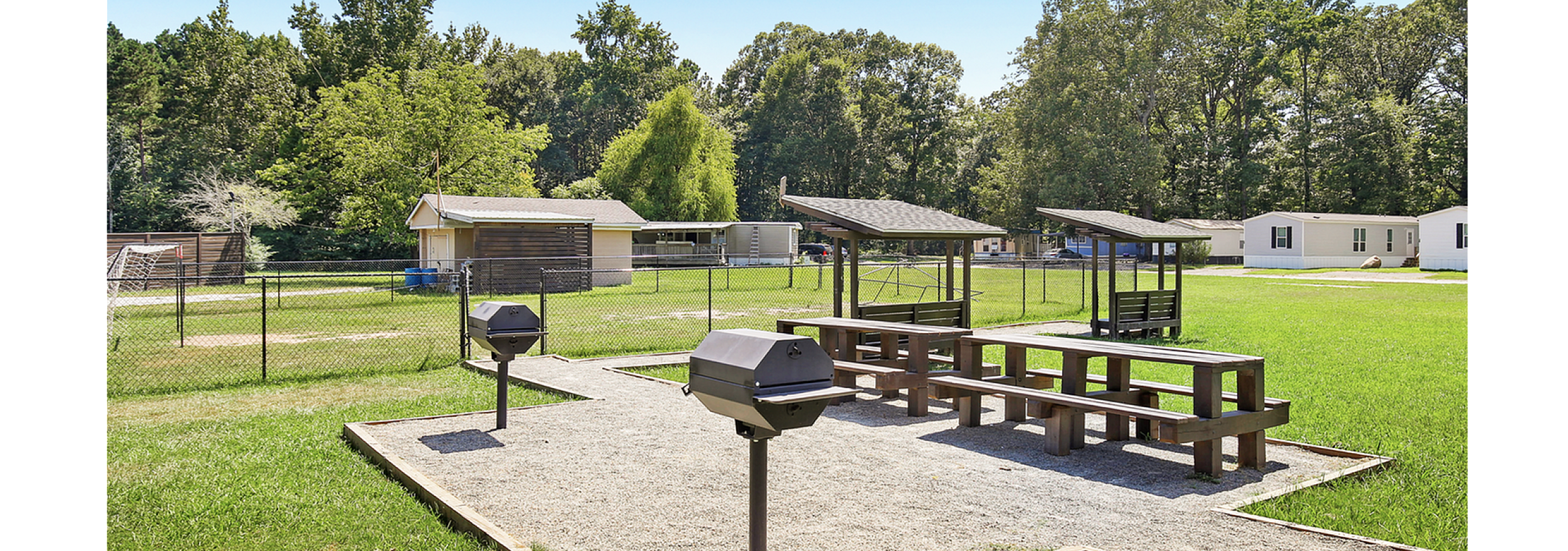 Inviting outdoor barbecue area with sleek grills and picnic tables, perfect for gatherings amidst a lush green lawn and serene surroundings.
